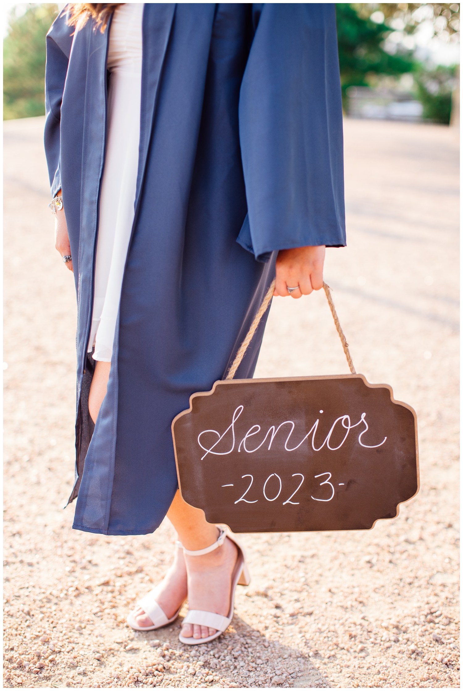 detailed image of a girls hands holding senior sign in navy graduation gown