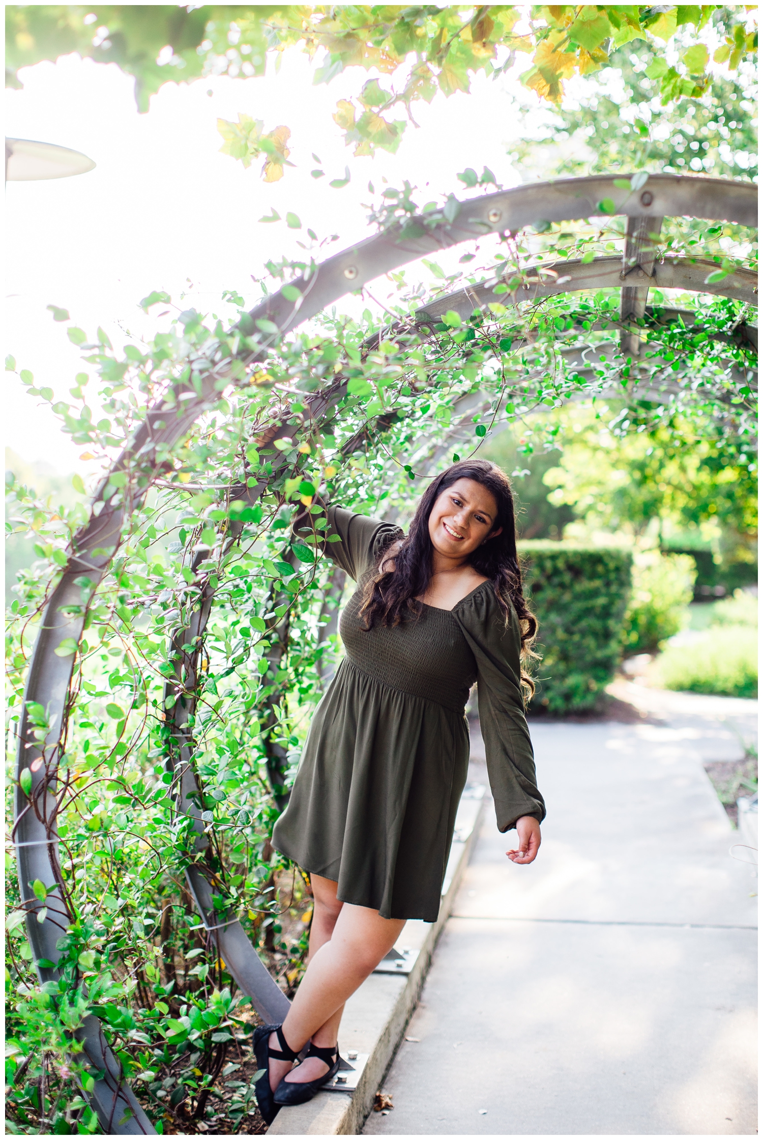 Houston senior girl in dark green dress hanging on archway with vines outdoors