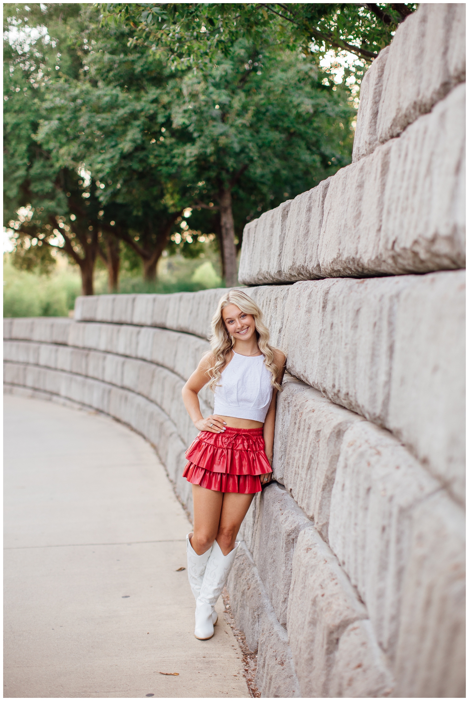 girl in white top and white boots and pink skirt leaning on gray wall for chic Houston senior pictures