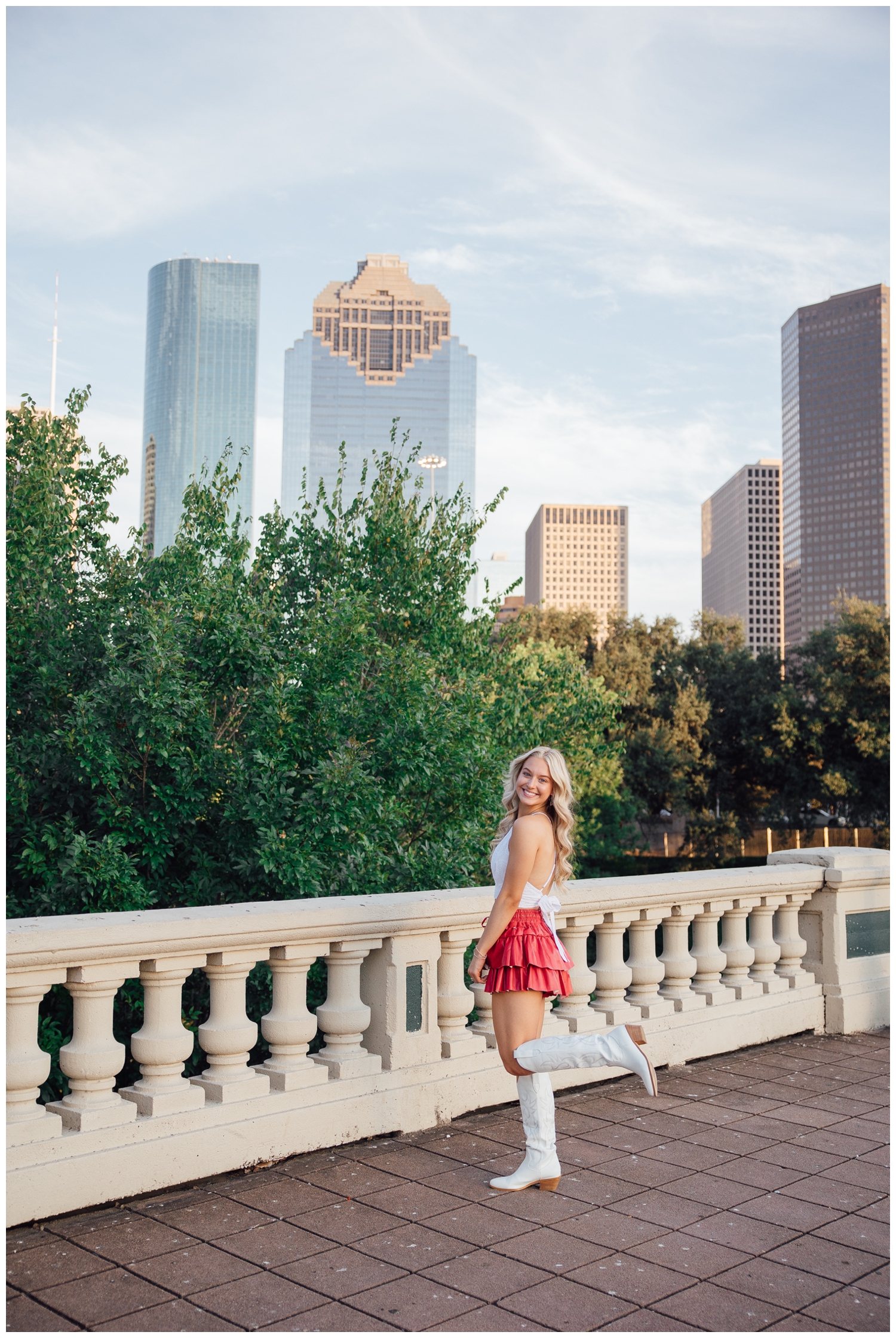 high school senior girl standing on Sabine Bridge Downtown Houston with pink skirt, white boots and white shirt