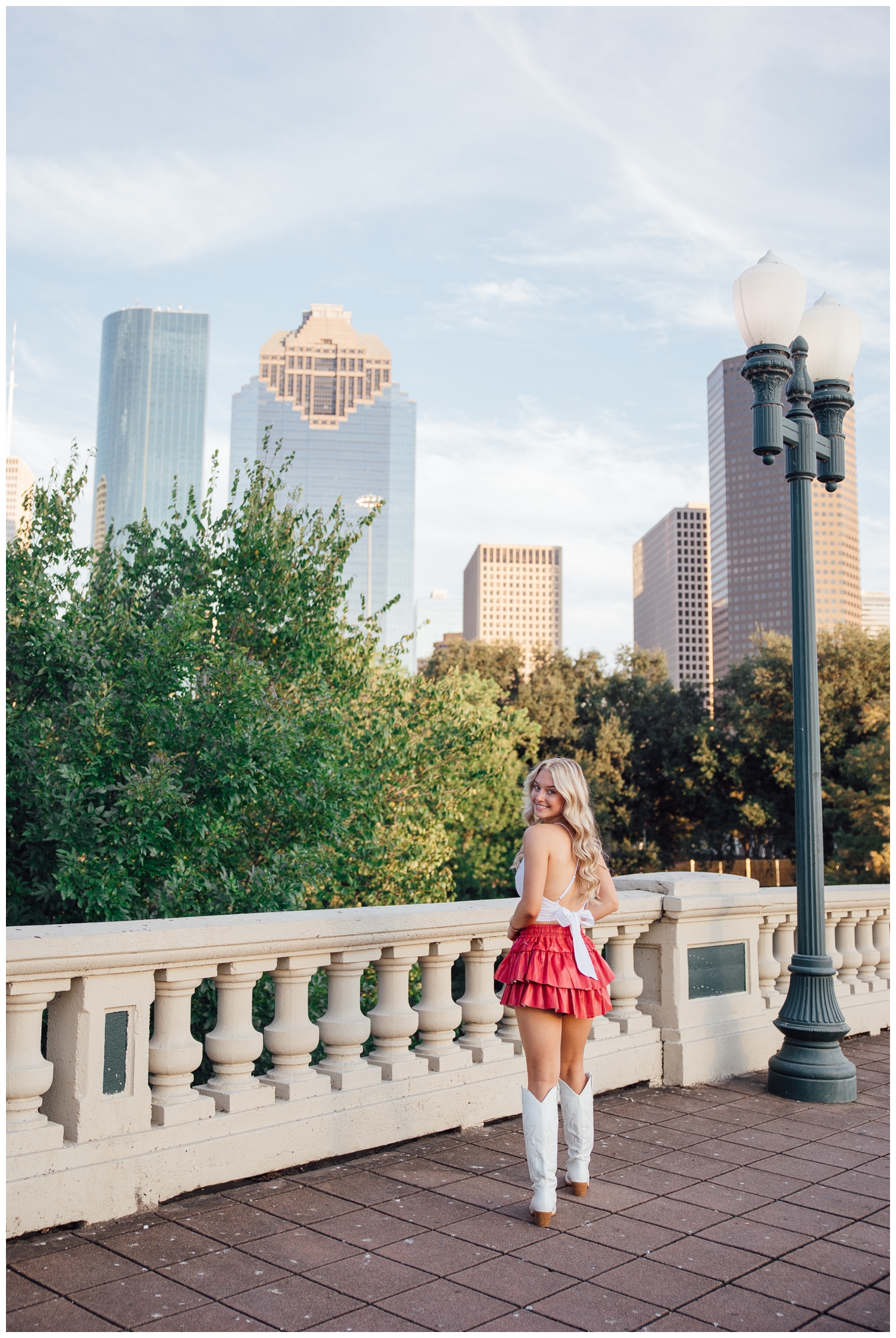 Chic Houston senior pictures downtown skyline girl in white top, pink ruffled skirt and white boots