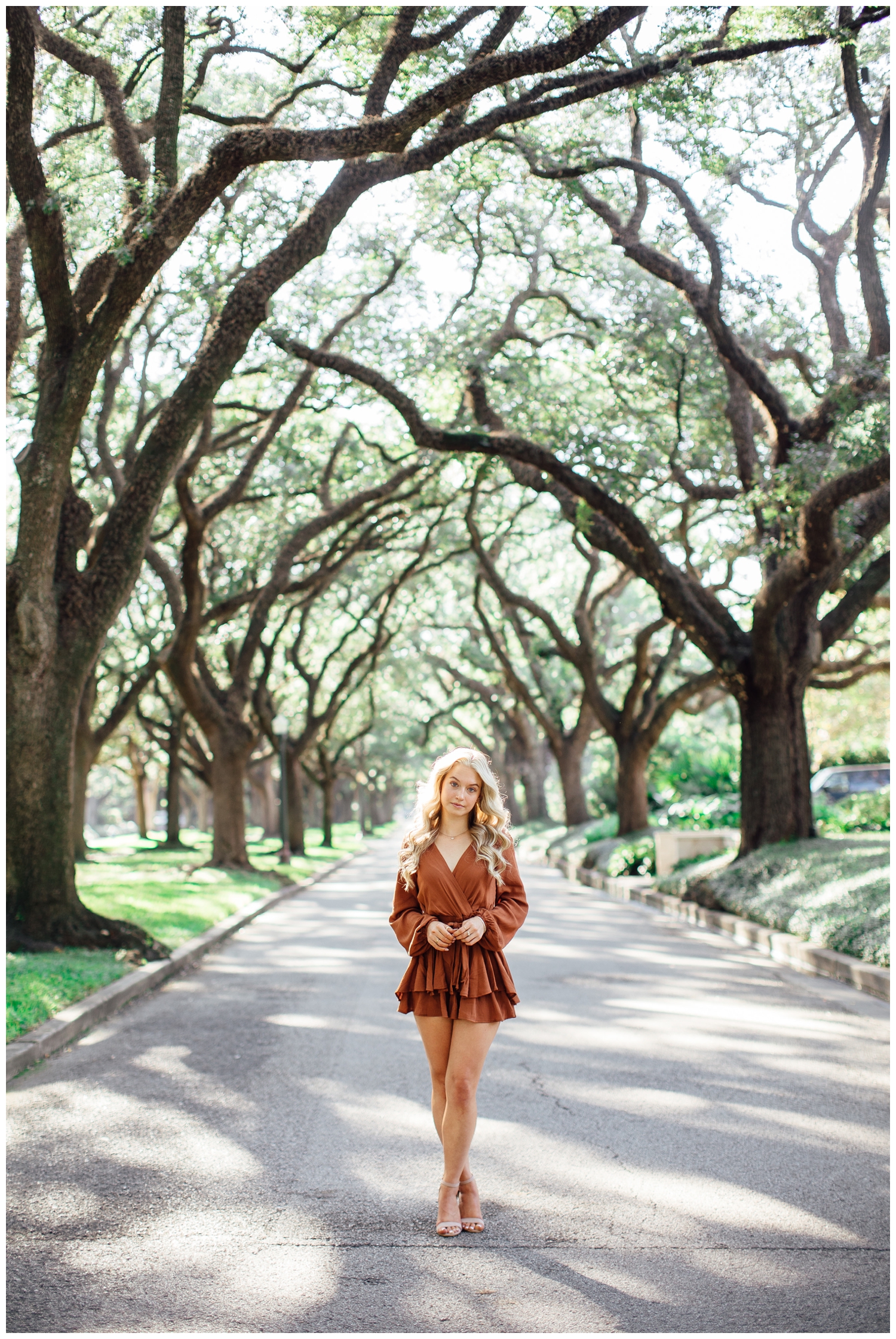 girl standing outdoors in tree line in rust romper with hands crossed