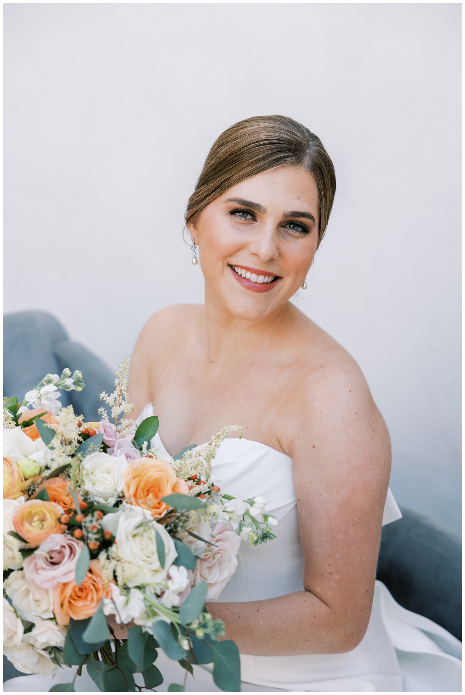 bride smiling at camera holding bouquet seating inside Iron Manor bridal suite