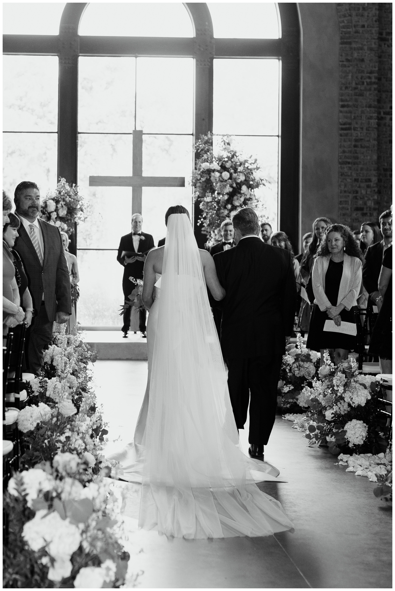 black and white image from behind of father and bride walking down Iron Manor ceremony aisle