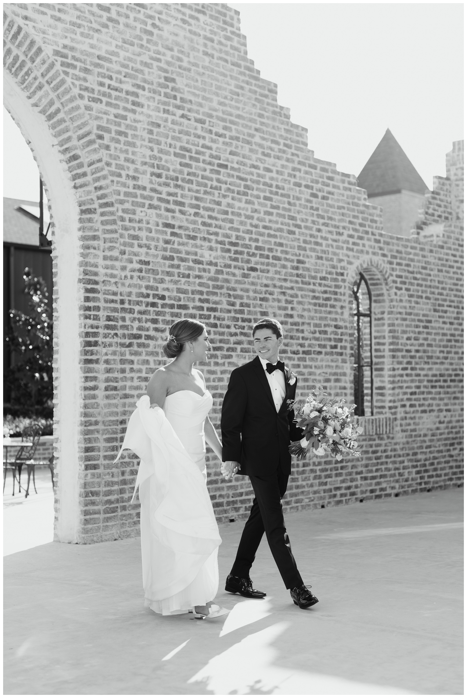 black and white image of bride and groom holding hands walking and looking at each other