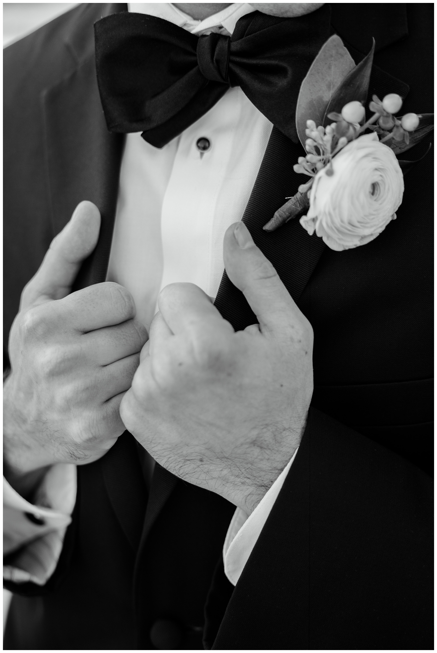 detailed black and white image of grooms hands holding his black tux jacket outside for elegant Iron Manor Wedding