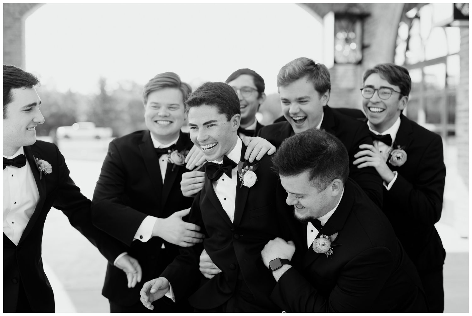 black and white image of groom surrounded by groomsmen laughing