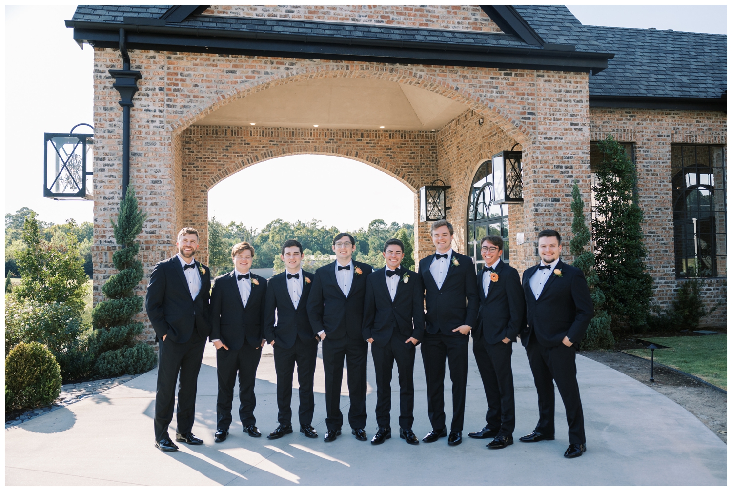 groom and groomsmen in black tuxes standing in a line outside Iron Manor Wedding venue