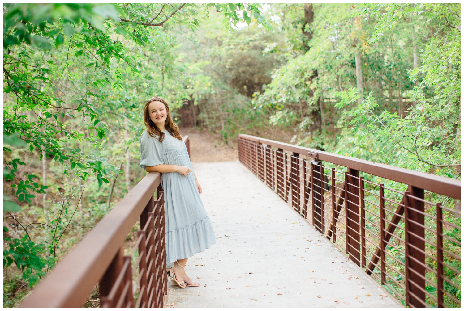 Houston high school senior girl in long blue dress leaning on a bridge at Houston Arboretum