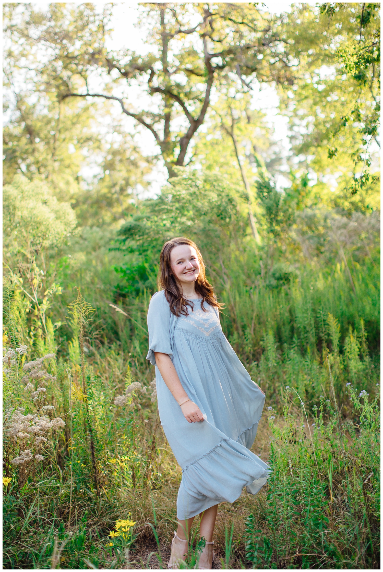 senior girl swaying in blue flowing dress in a field for