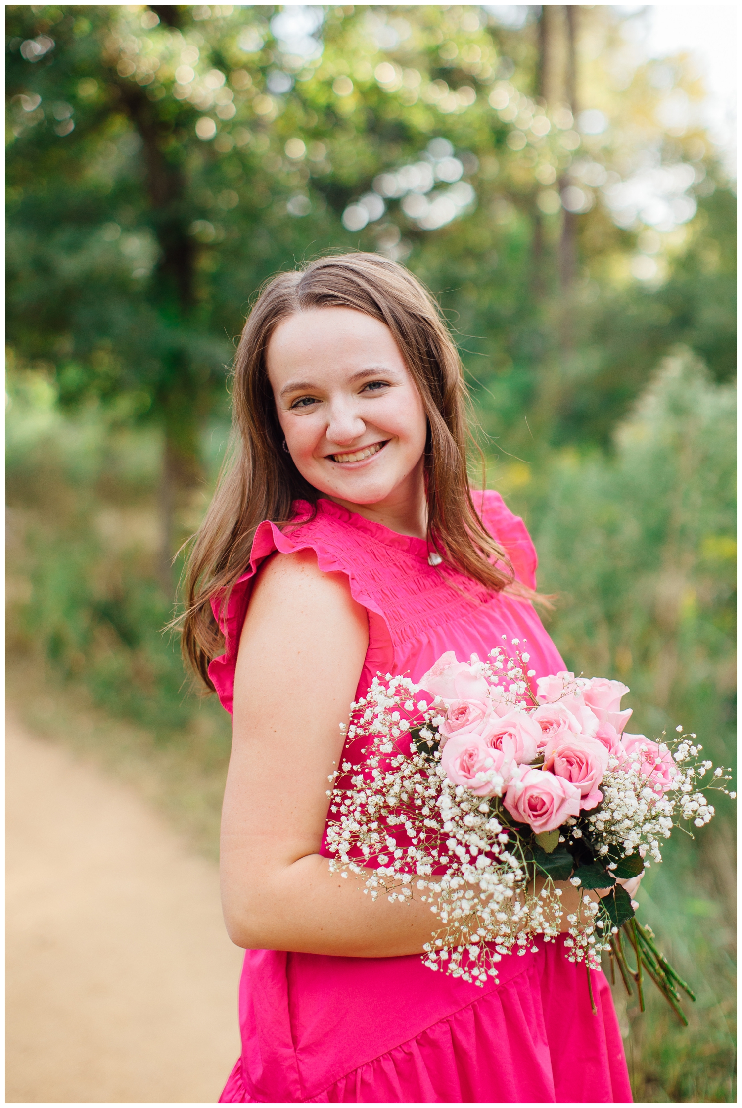 high school senior girl holding pink flowers in pink dress smiling for Houston senior photos with flowers