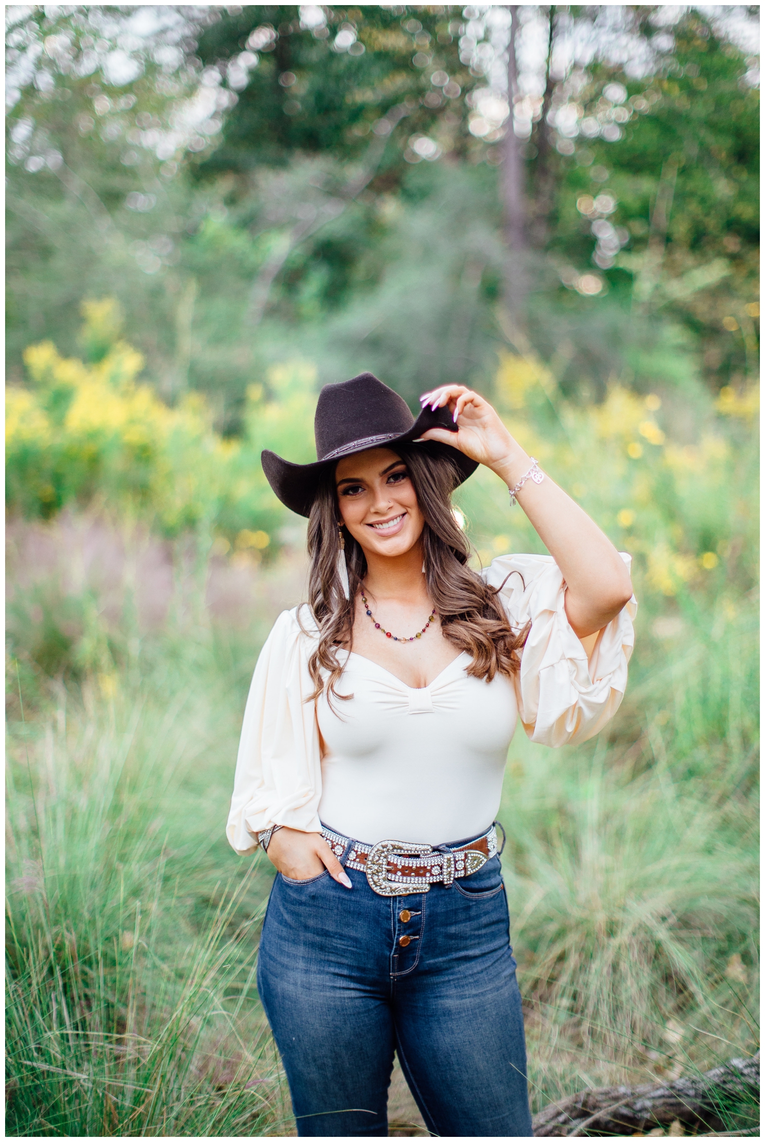 bold senior portraits in Houston Arboretum with girl standing in field tipping cowboy hat