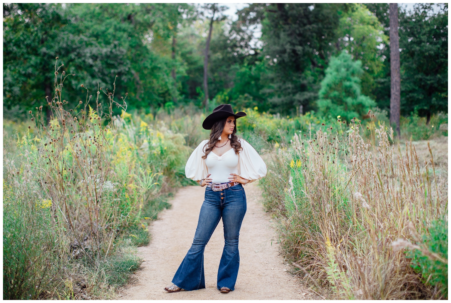 girl standing in pathway Houston Arboretum with hands on hips in jeans black cowboy hat