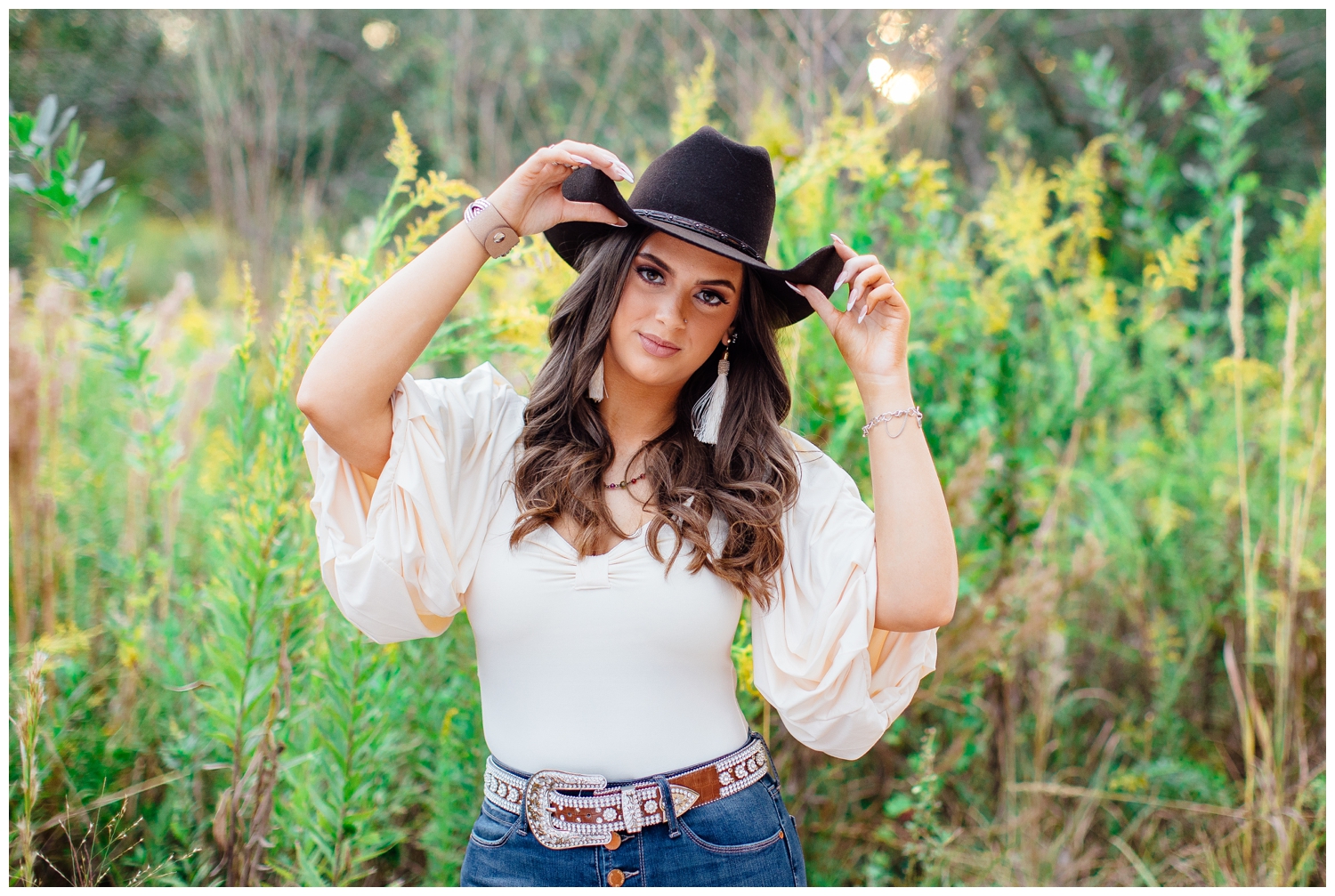 high school senior girl standing in field at Houston Arboretum holding black cowboy hat