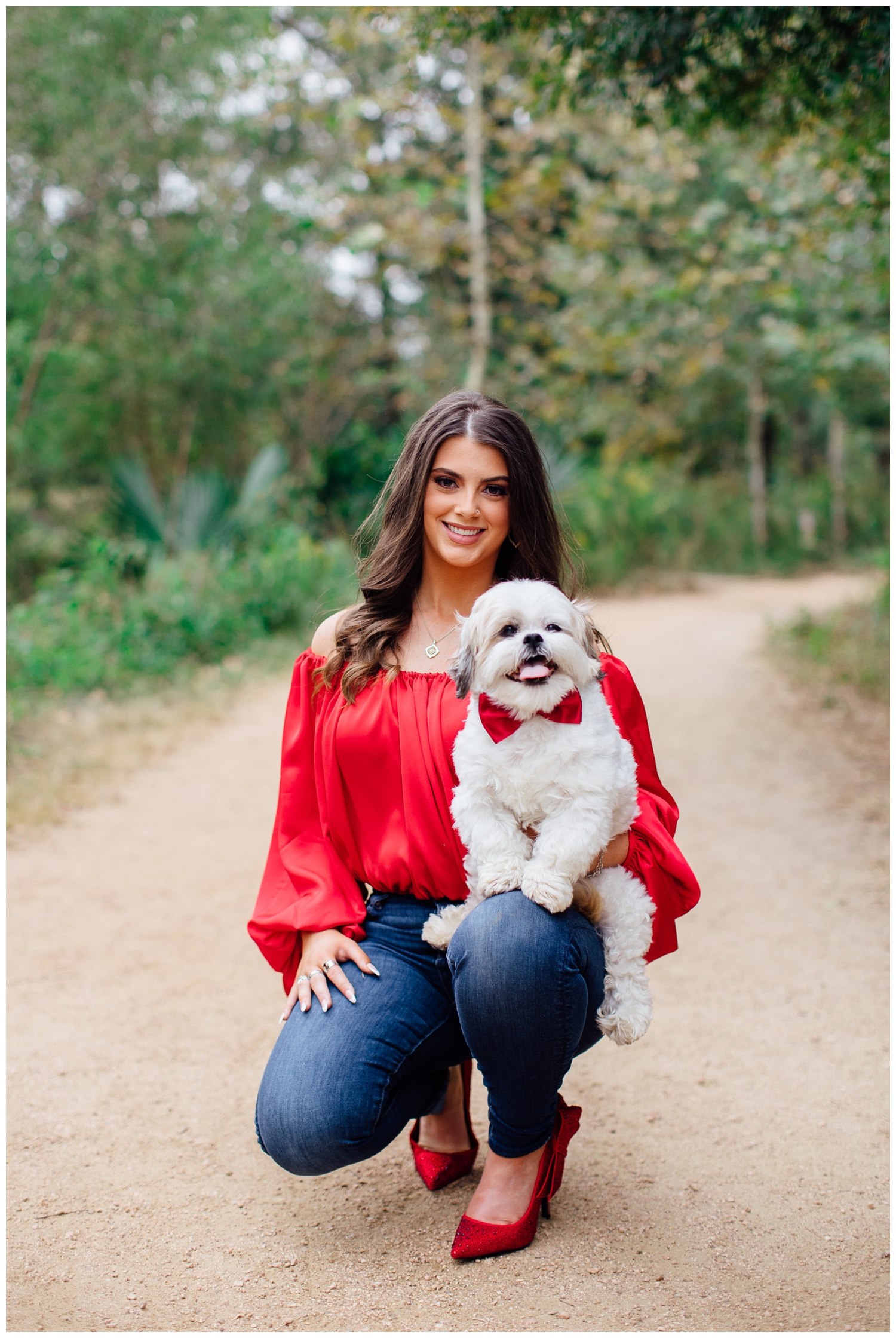 girl in red shirt and jeans holding white dog in red bow tie for bold senior portraits in Houston Arboretum