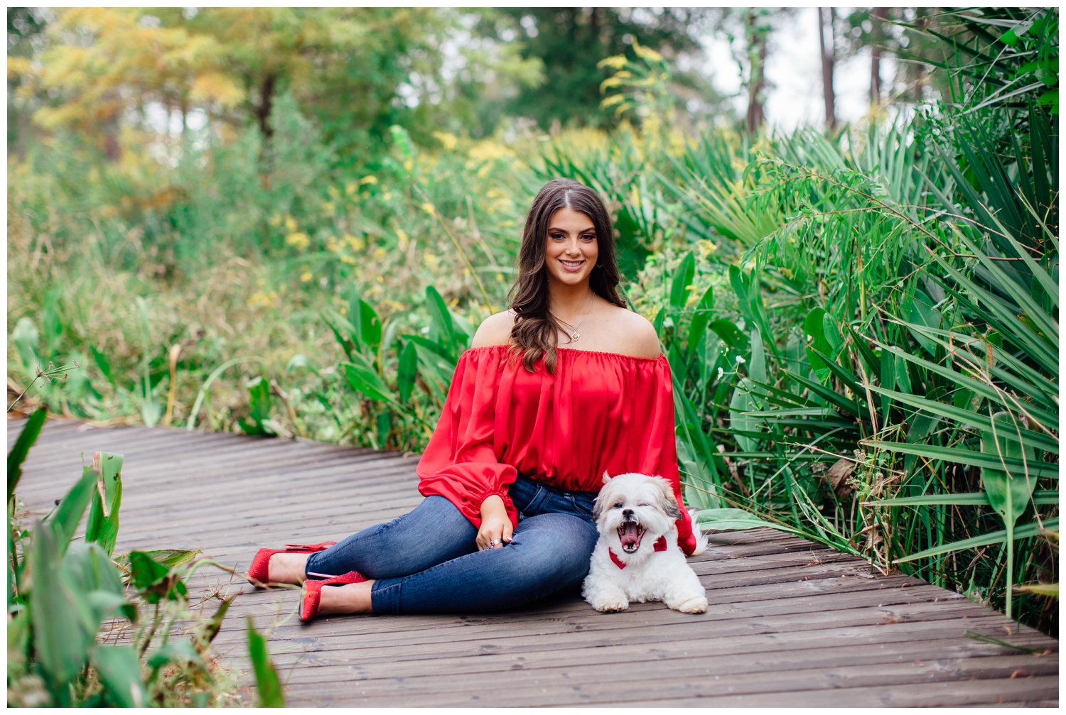 girl in red blouse and jeans with dog sitting bold senior portraits in Houston at Arboretum