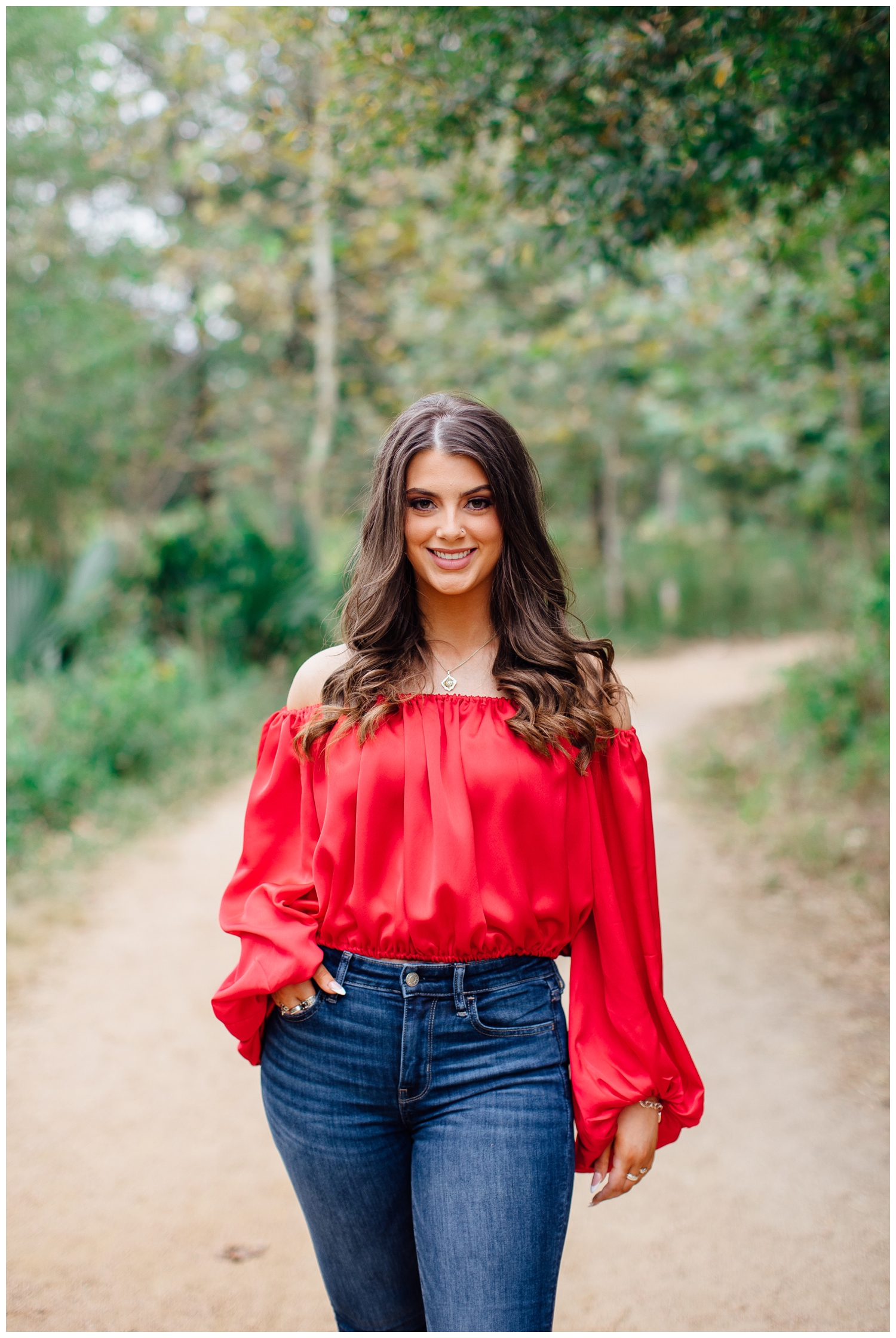 high school senior in jeans and red blouse smiling for bold senior portraits in Houston Arboretum