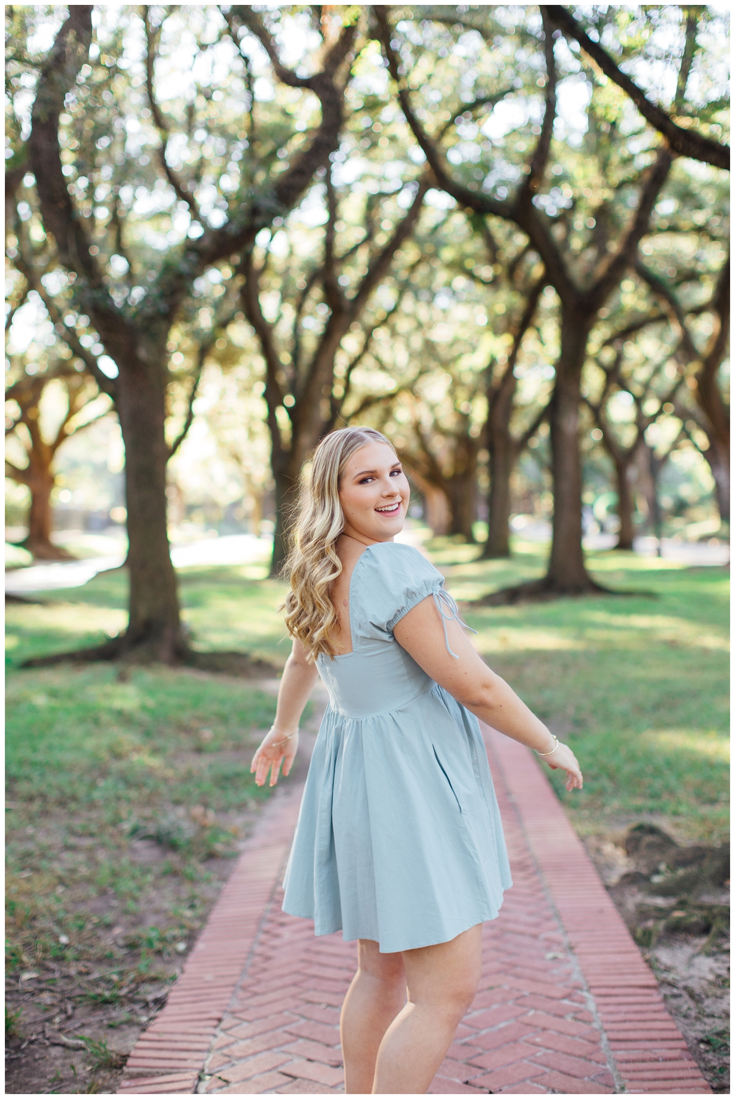 senior girl in blue dress twirling on pathway between trees in Houston