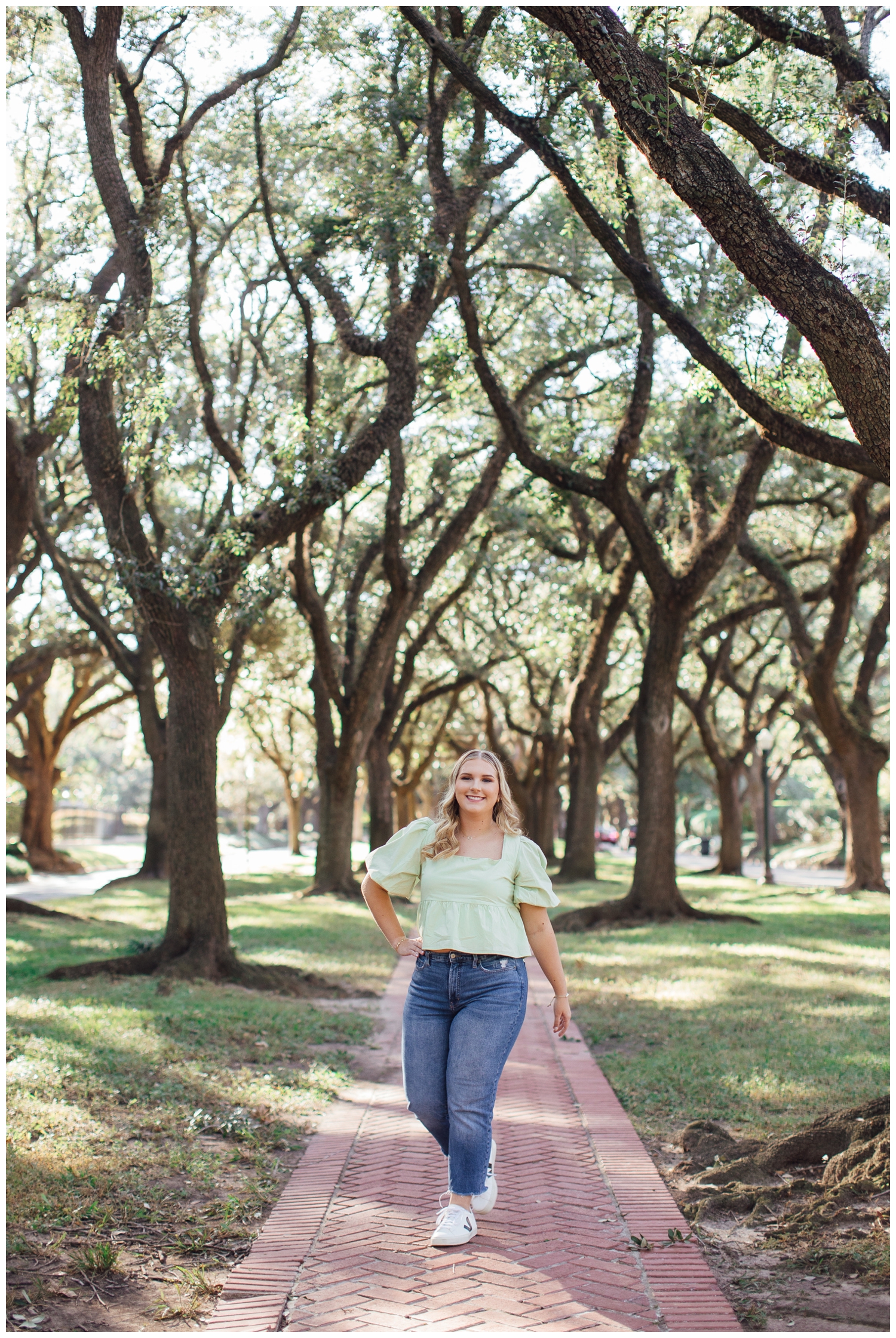 girl in jeans and green blouse walking between the trees at North South Blvd for senior pictures in Houston