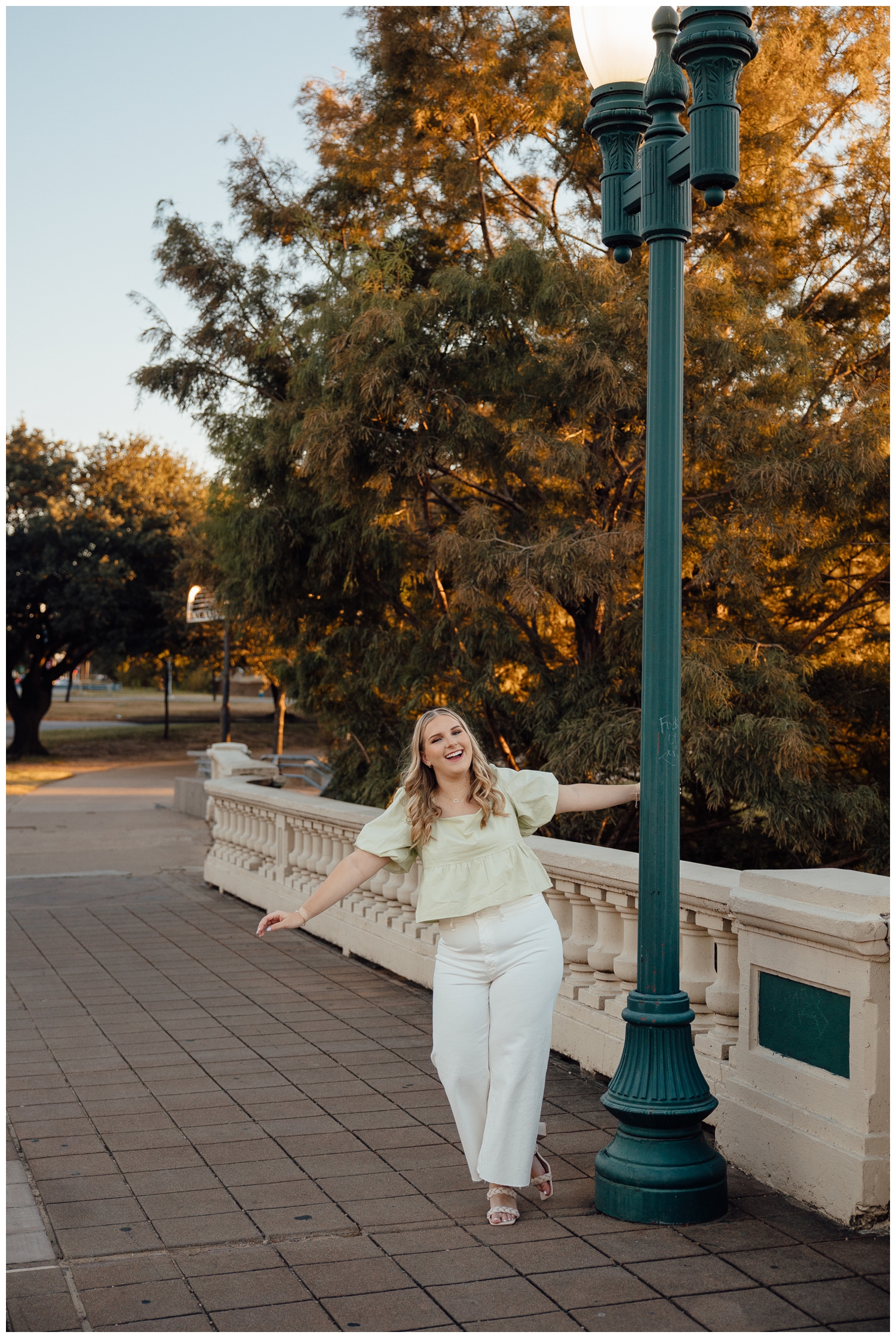 high school senior girl in white pants and sage blouse hanging off lamp post Sabine Street Bridge downtown Houston
