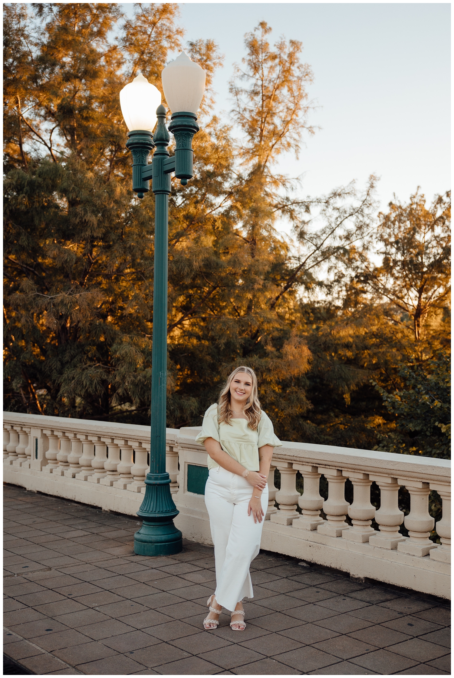 girl with arms crossed standing on Sabine Street bridge in white pants and colored top for cute senior pictures in Houston