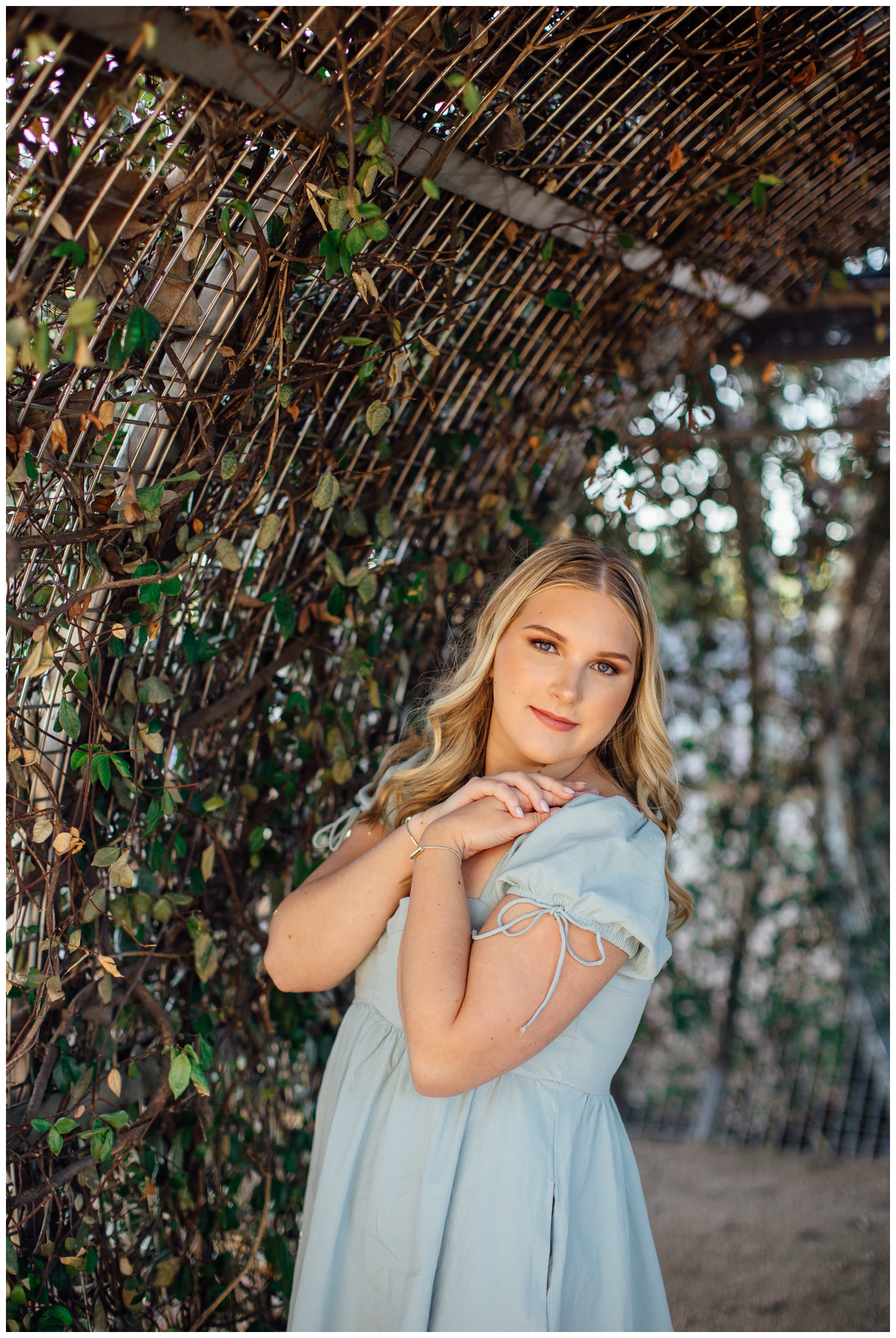girl in blue dress with hands on shoulders under ivy arch for cute senior pictures in Houston downtown