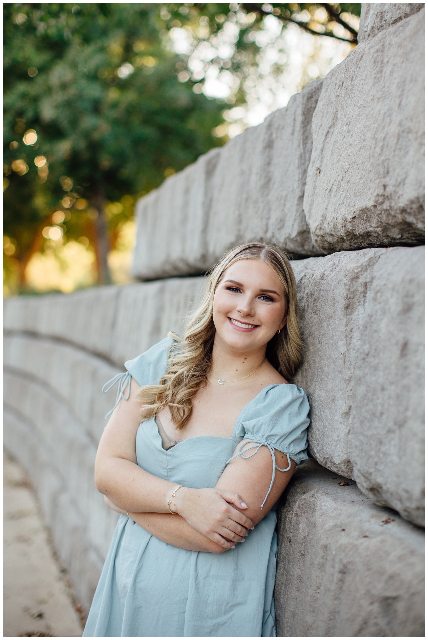 high school senior girl leaning against gray wall smiling with arms crossed for senior pictures in Houston