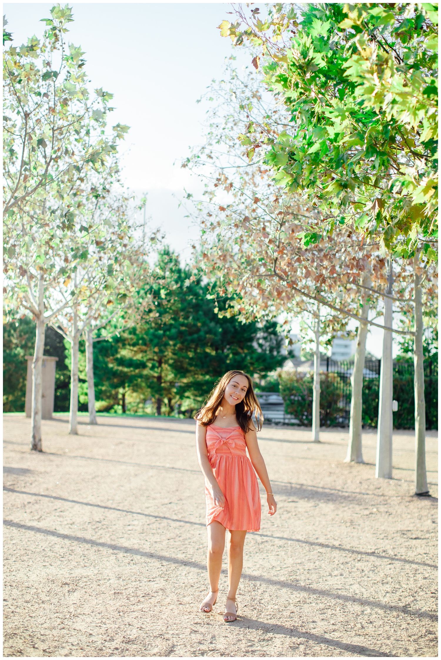 high school senior girl in coral sundress walking in tree line for downtown Houston senior picture