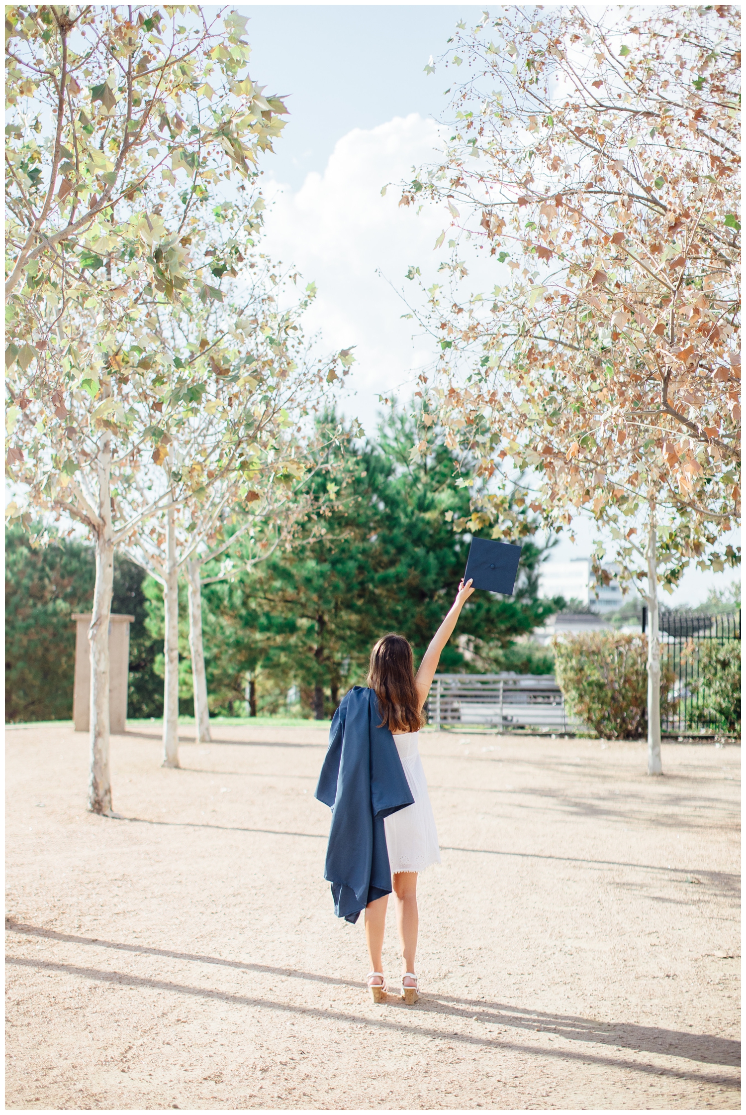 girl walking away from camera in blue graduation gown and cap held in the air