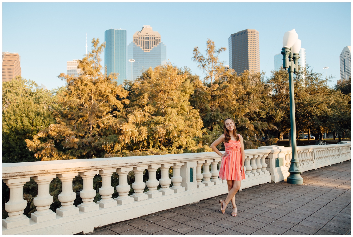 girl in coral dress standing on Sabine Street Bridge with hands on hip and Houston skyline in background