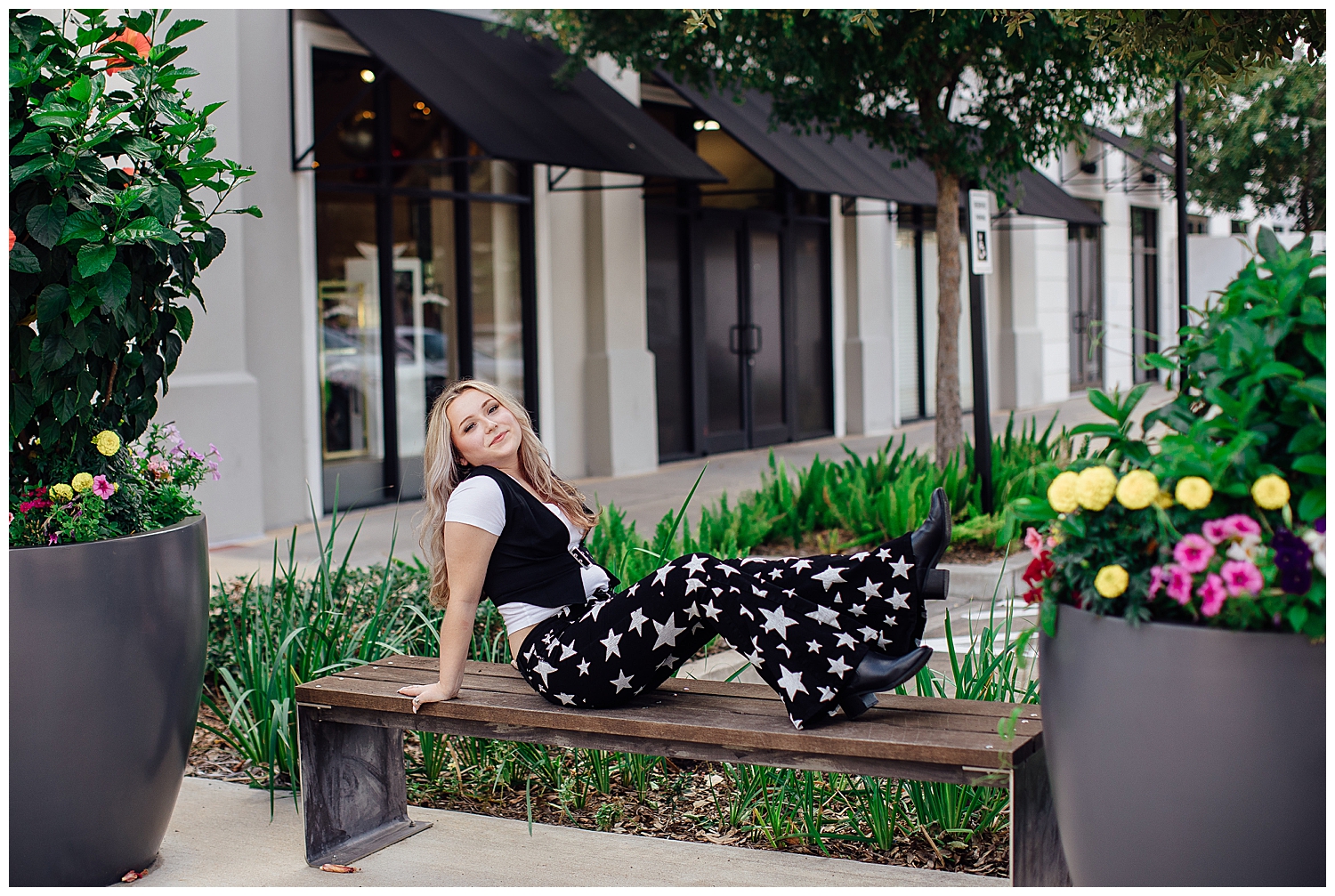 girl in black pants with stars, white shirt sitting on a bench with legs out for modern Houston senior photographer