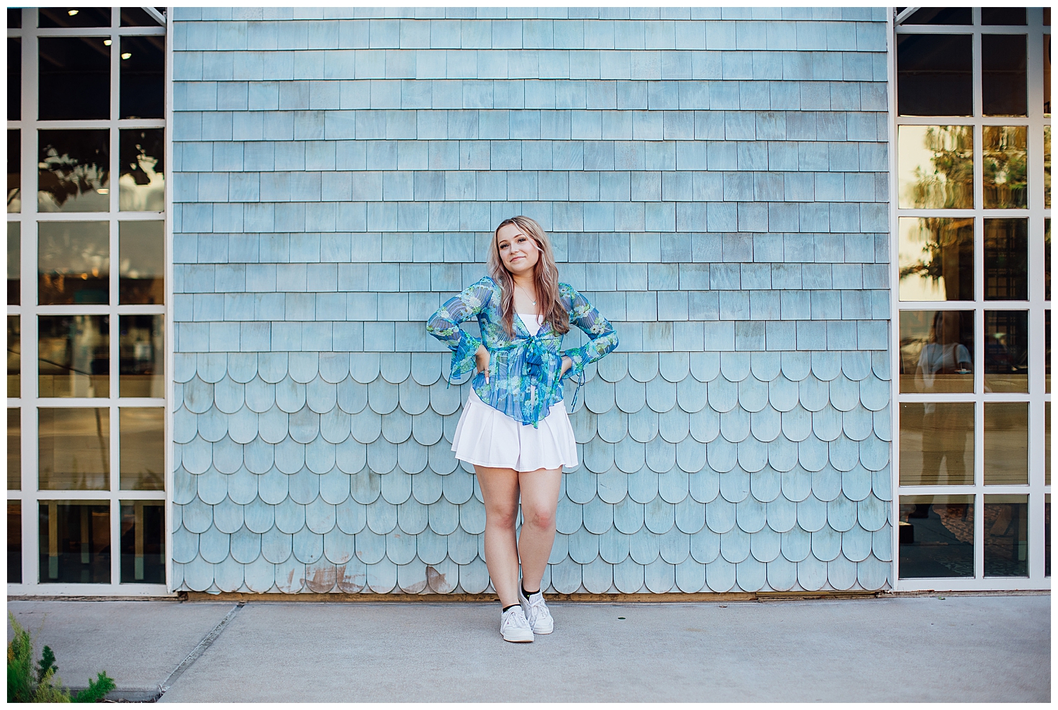 Houston high school senior in white skirt, white sneakers and blue shirt leaning against blue wall