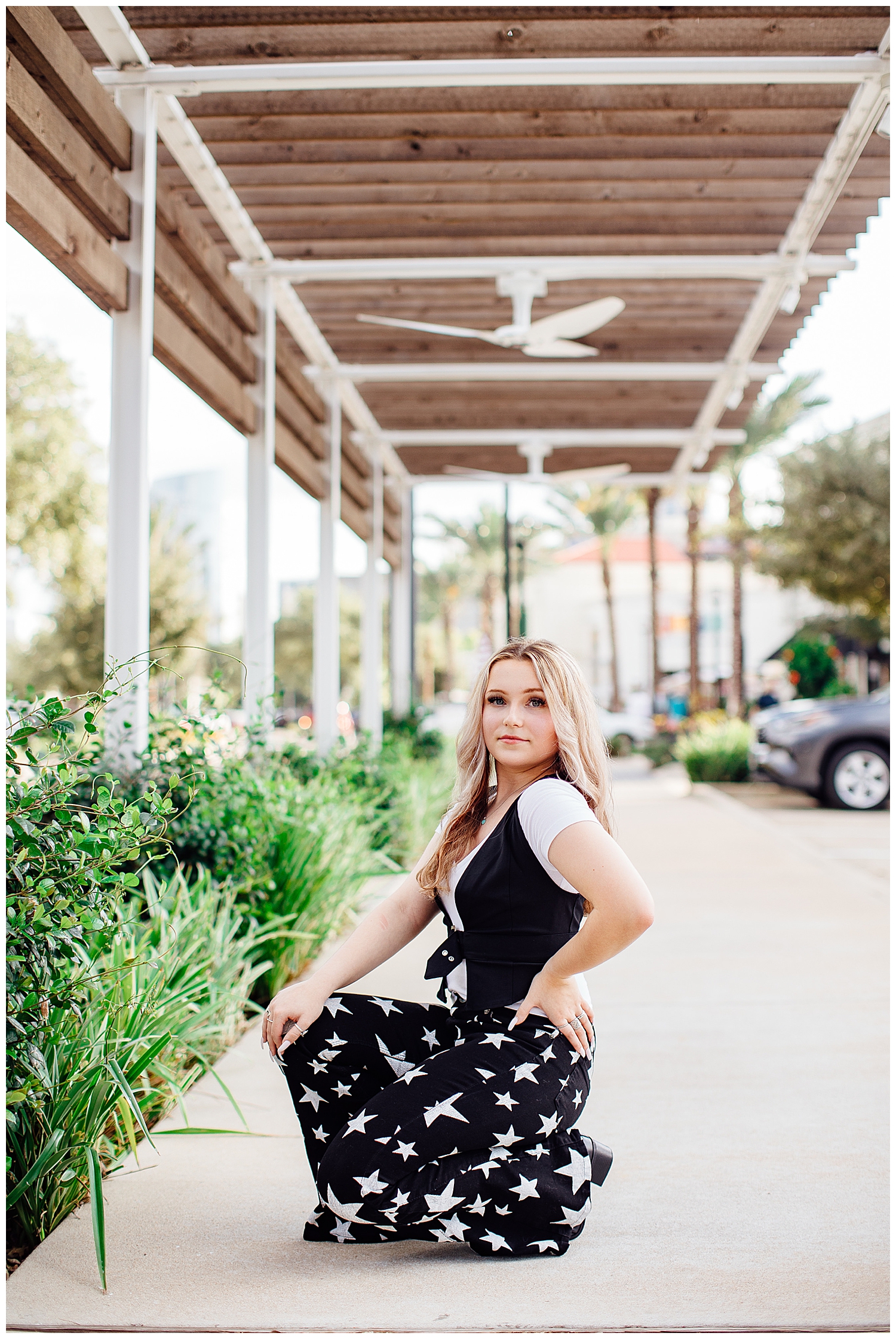high school girl kneeling at Uptown Park in black star pants for modern Houston senior photographer
