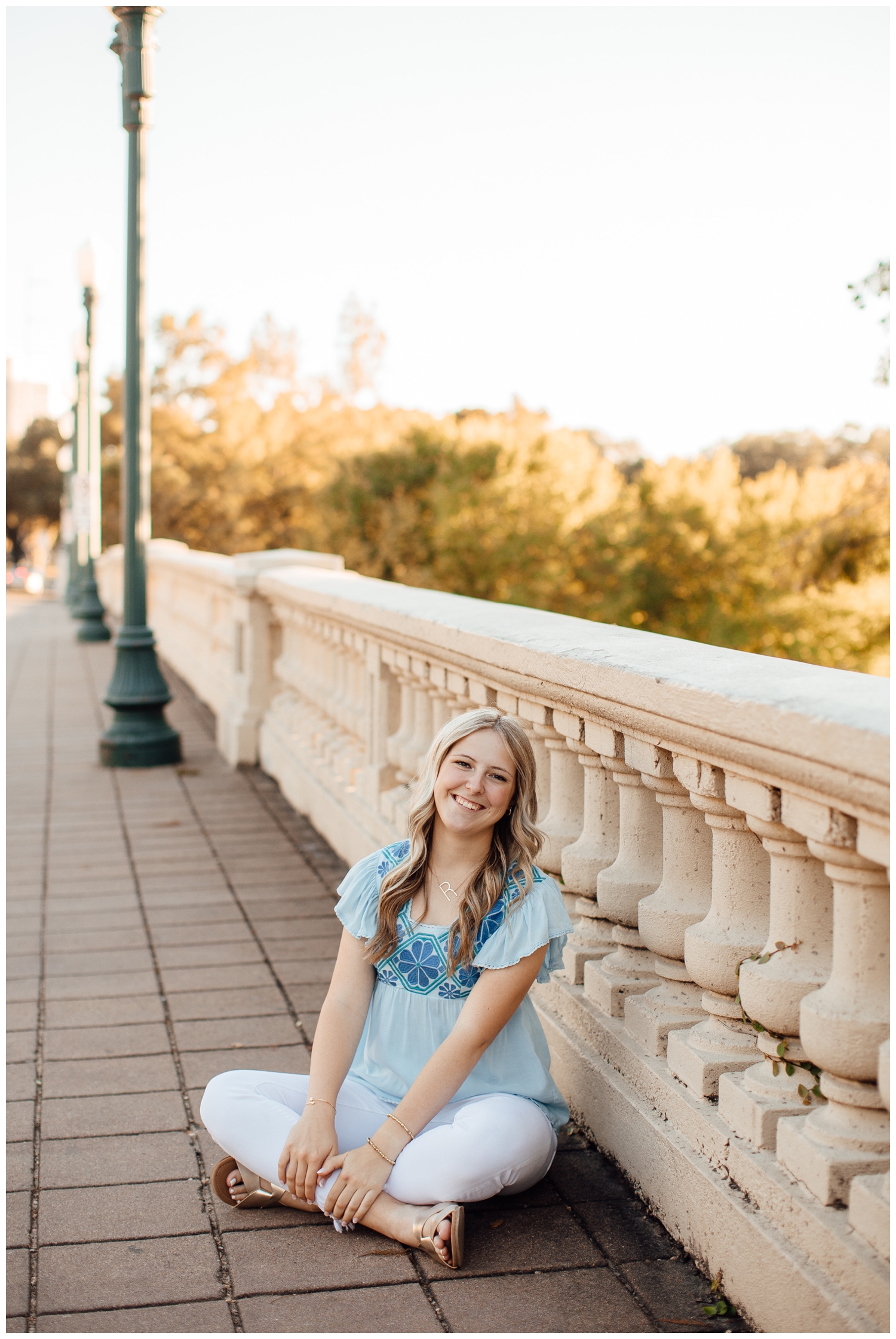 girl in white pants and blue blouse sitting on Sabine Street Bridge for Outdoor Houston senior photography