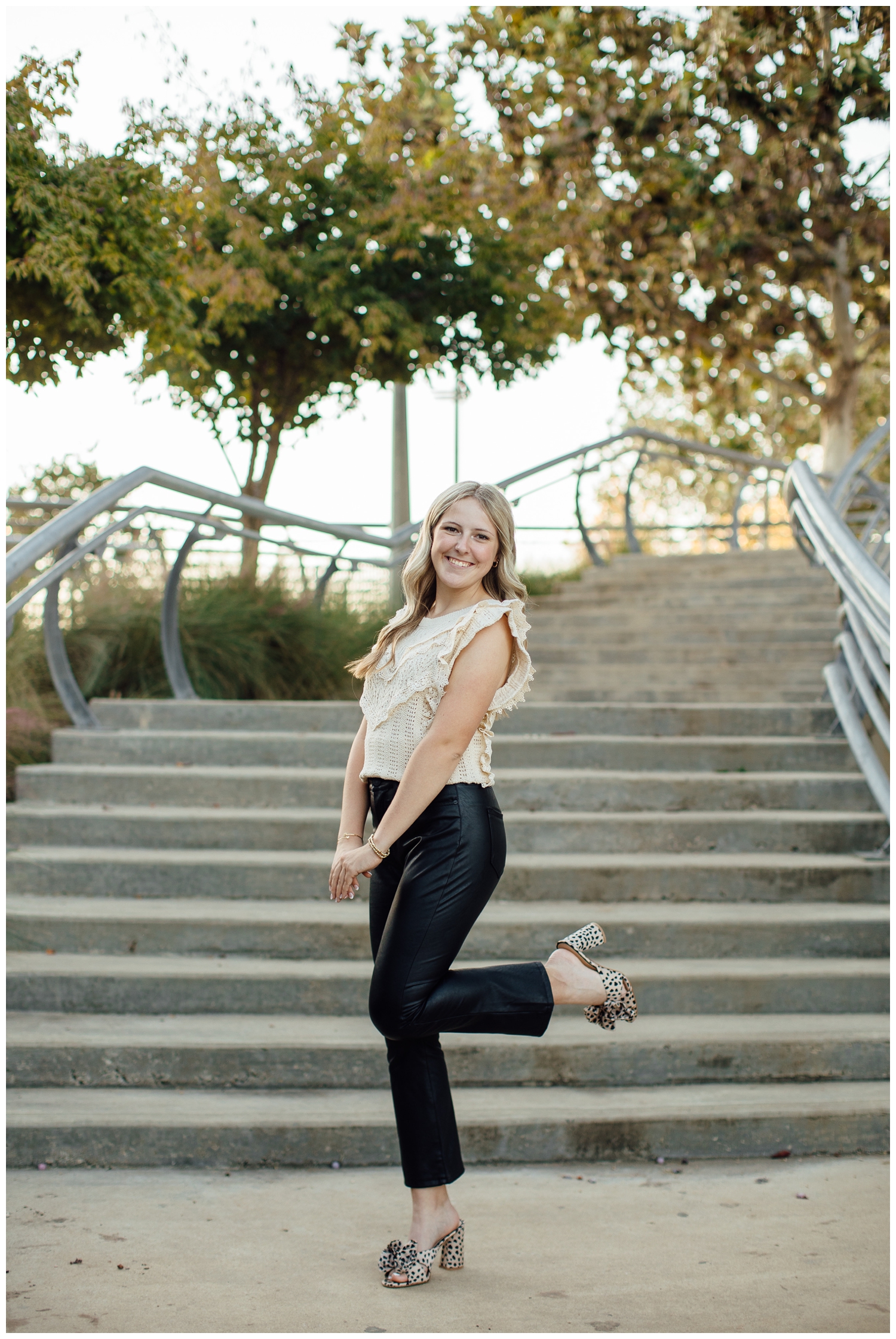 high school senior girl in black leather pants, cream shirt and heels standing on staircase for Outdoor Houston senior photography