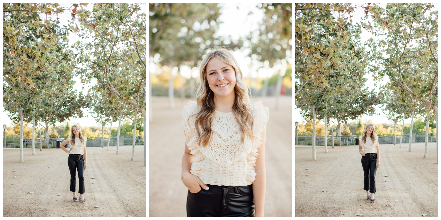 high school senior girl in black leather pants, beige sweater for Outdoor Houston senior photography walking in tree line