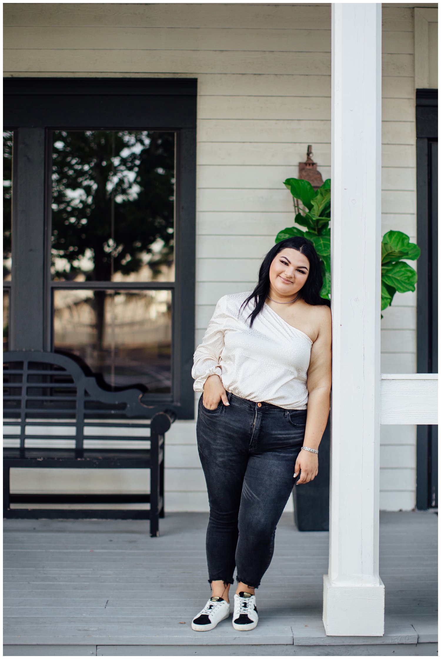 girl leaning against white column outdoors wearing black jeans and cream shirt