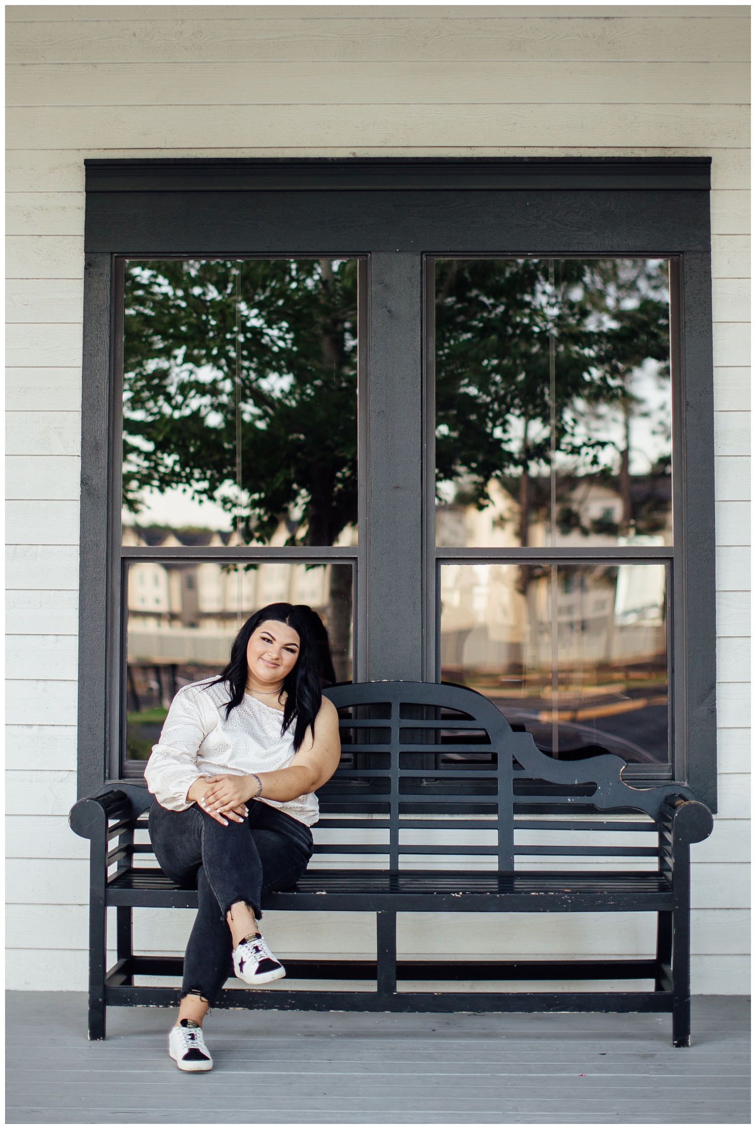 girl sitting on black bench in cream shirt black jeans for for senior photographer in Cypress outside Cy-Hope
