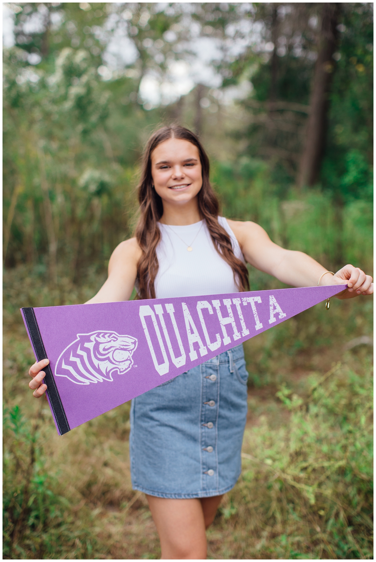 senior girl holding purple Ouachita banner in field at Houston Arboretum