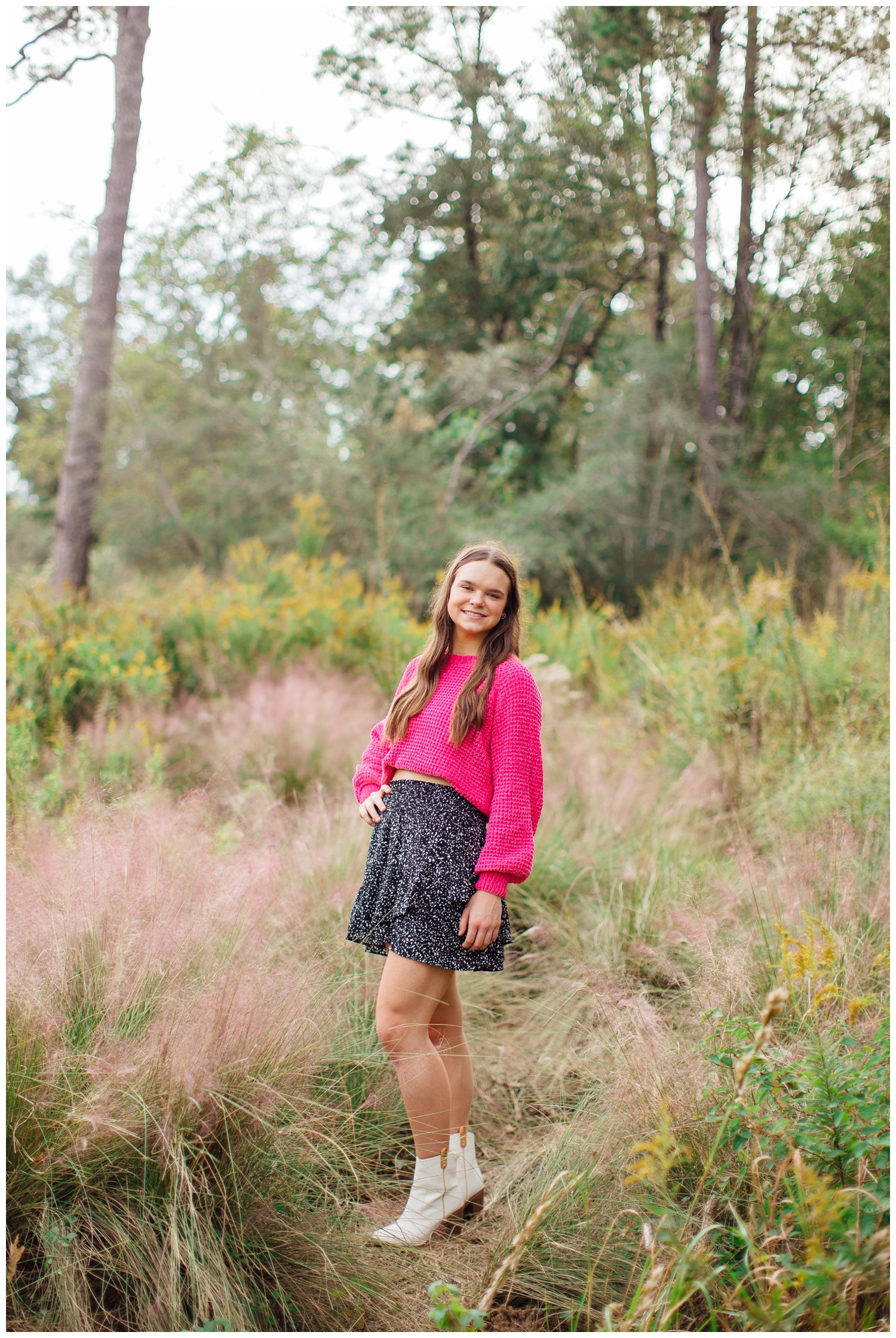 girl in hot pink shirt and black skirt standing in field for senior pictures Houston Arboretum