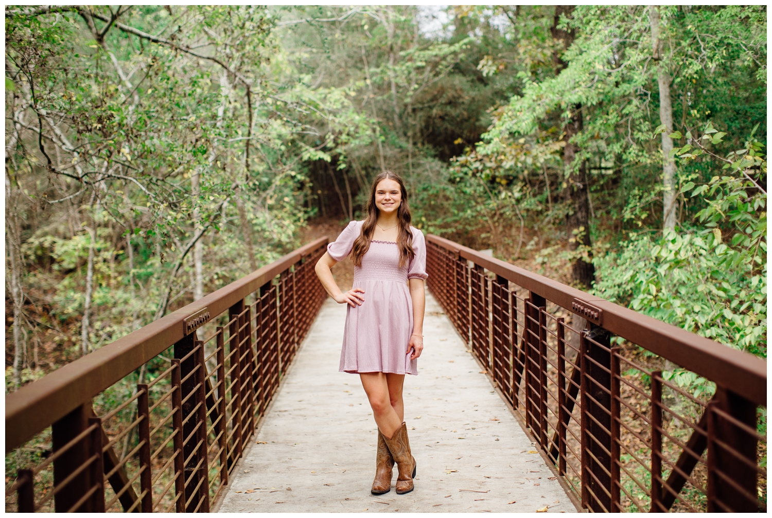 high school senior girl in pink dress and brown boots with hand on hip standing on bridge at Houston Arboretum
