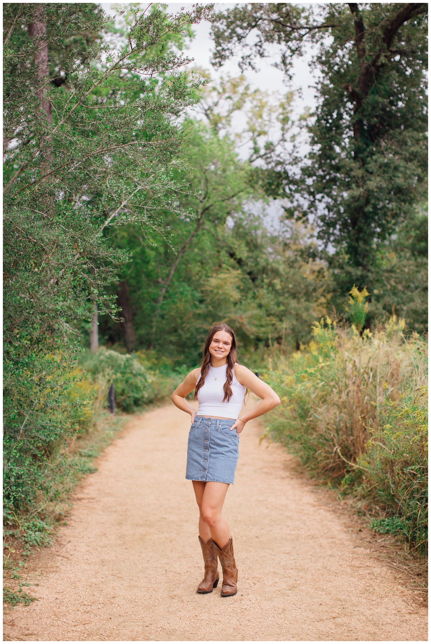 high school senior girl in white shirt, denim skirt standing on a Houston pathway with hands on hip