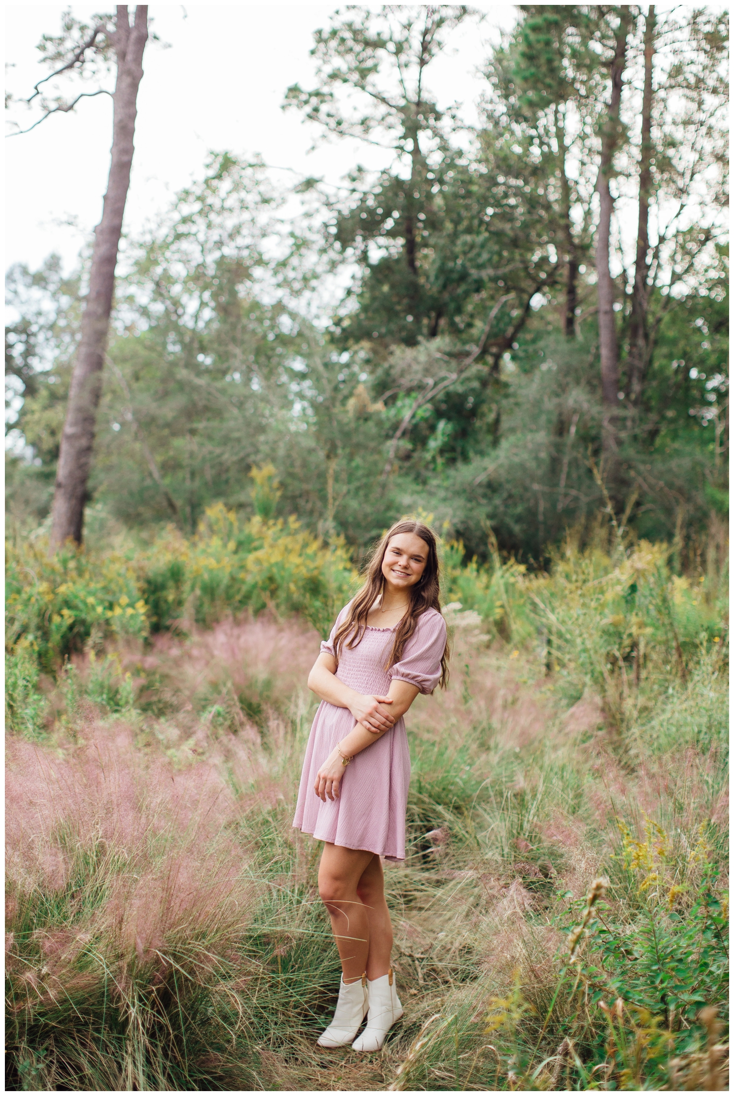 girl in pink dress standing in field with arm crossed for senior pictures Houston Arboretum
