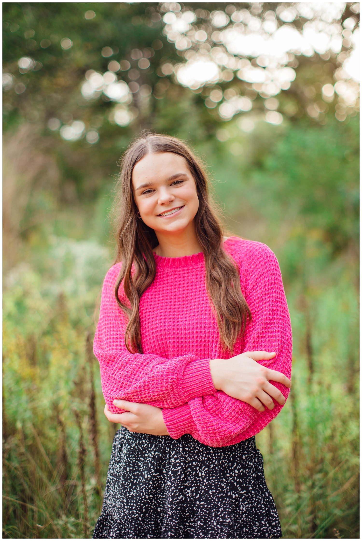 high school senior girl standing with arms crossed in hot pink shirt in field in Houston Texas