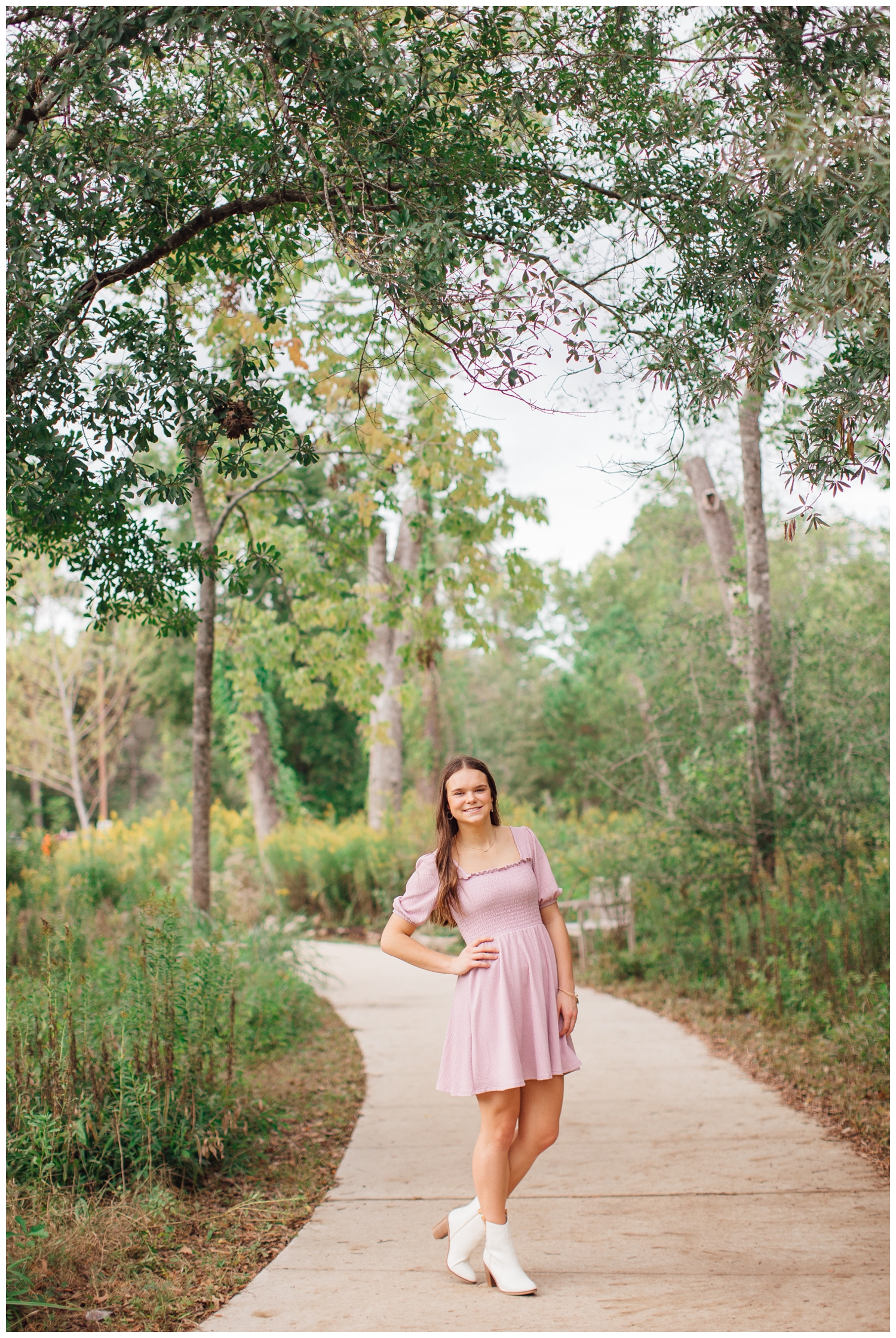 senior girl in pink dress standing with hand on hip at Houston Arboretum
