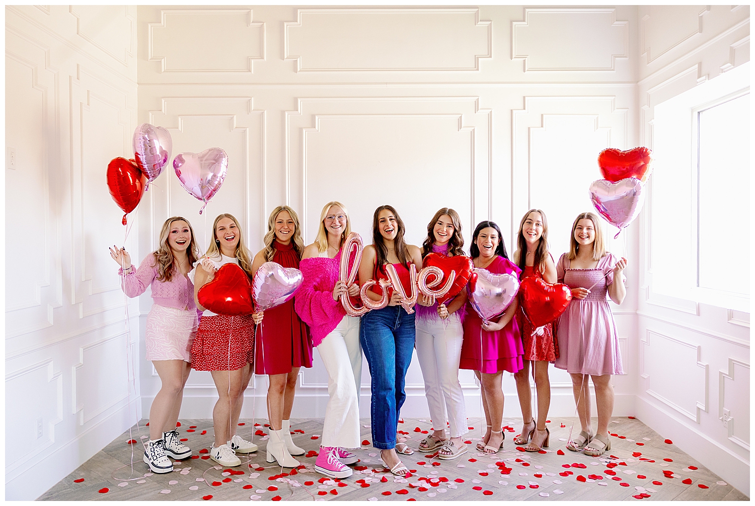 Valentine's Day Senior Photoshoot for Reed Gallagher Photography with ten girls in pink, red and white standing in front of white wall with balloons