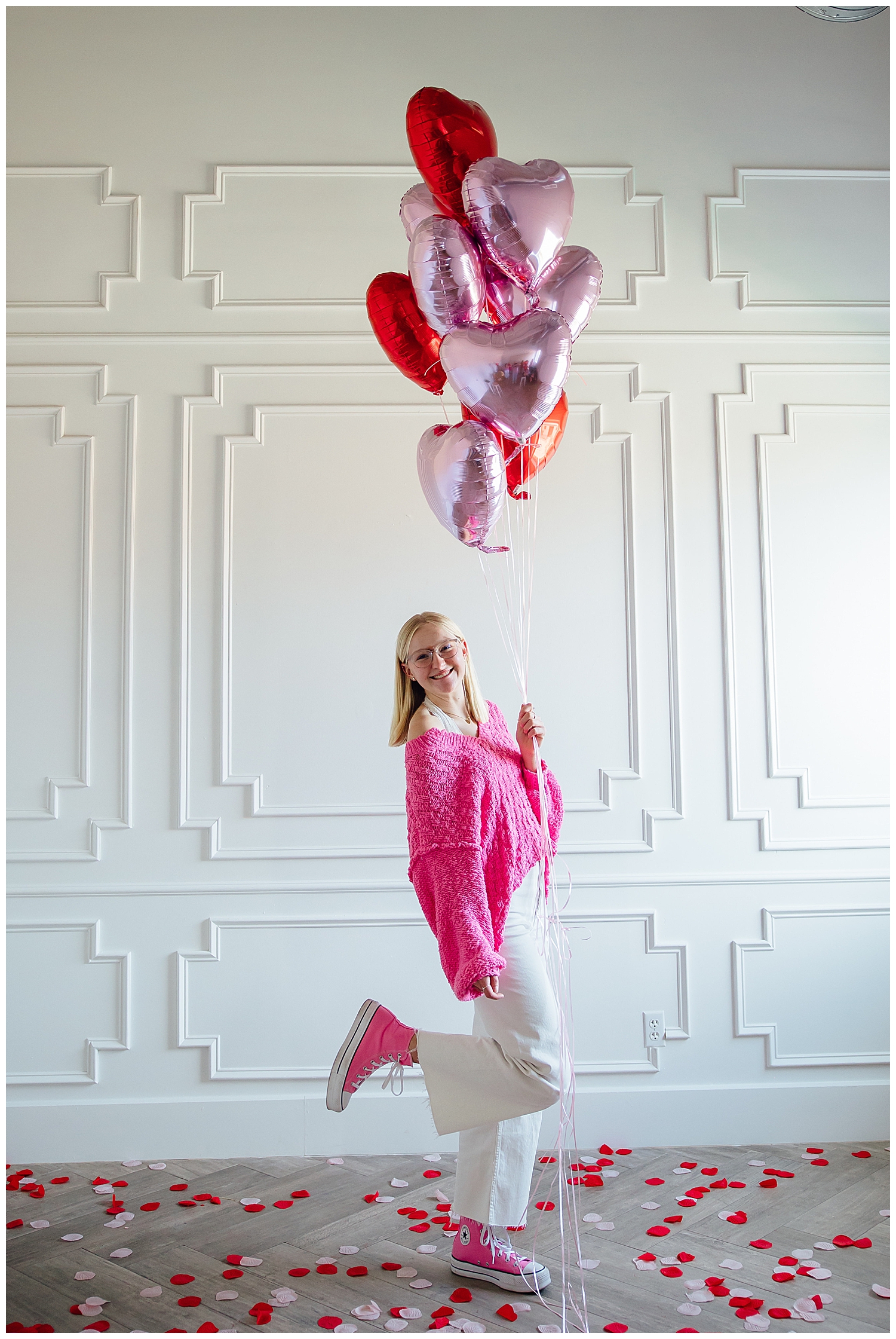 high school senior girl in hot pink sweater, pink converse and white pants holding heart balloons