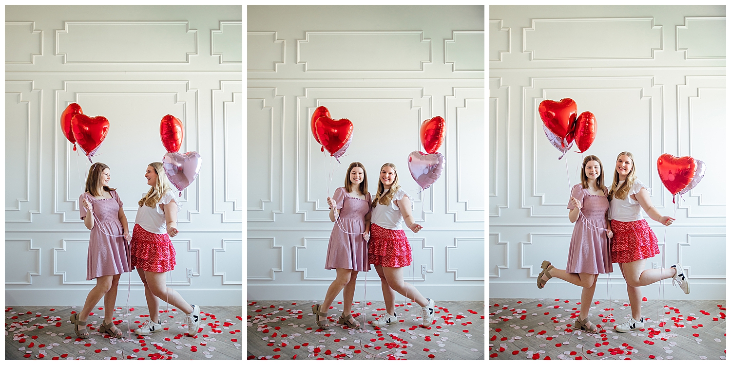 two high school girls in pink and white standing on rose petals holding heart balloons Valentine's Day Senior Photoshoot