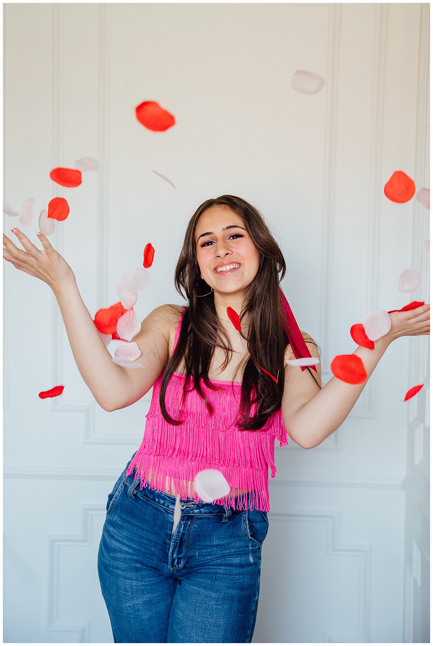 high school senior girl in hot pink and jeans throwing up rose petals for Valentine's Day Senior Photoshoot