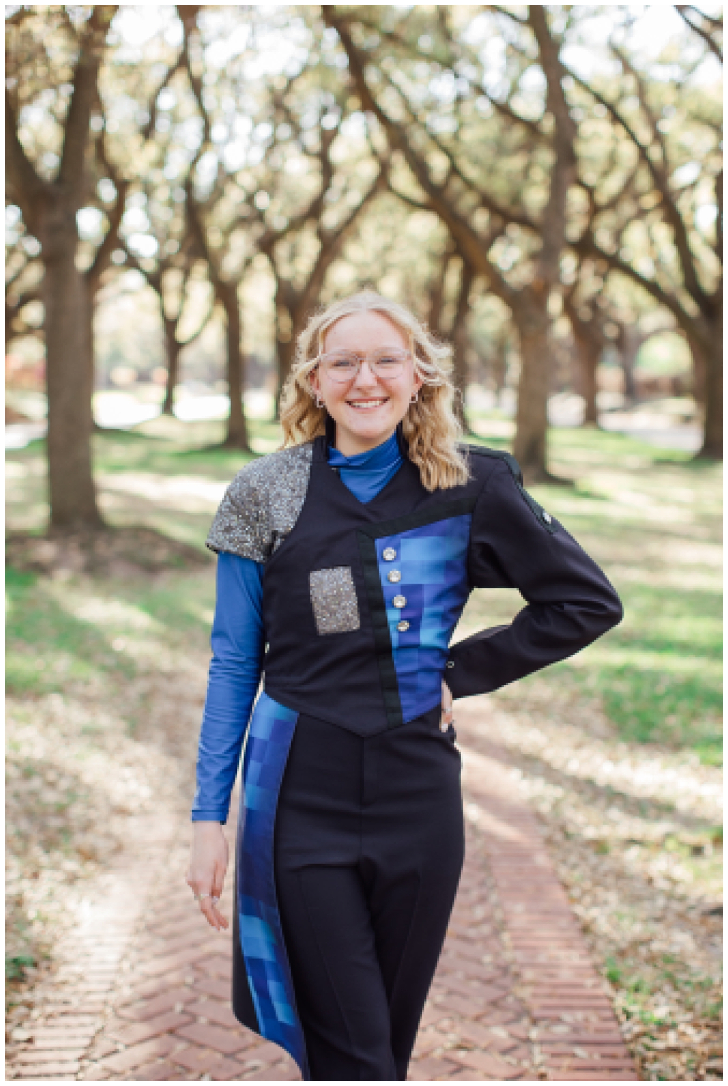 high school senior girl standing between tree line in blue band uniform